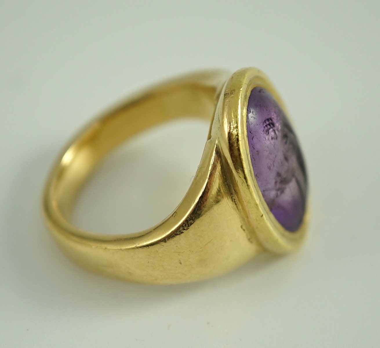 A Roman oval intaglio amethyst, carved with a figure with staff and pedestal, set in a later heavy gold ring mount